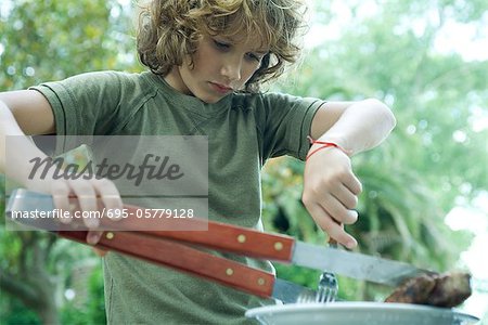 Boy picking up piece of meat from plate