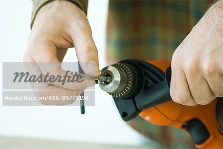 Man adjusting drill bit, cropped view of hands