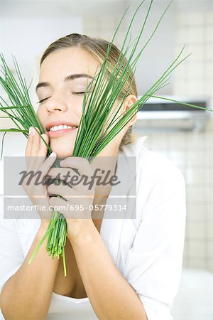 Young woman holding chives up to face, eyes closed