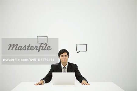 Businessman sitting with laptop computer, blank word bubbles on wall behind him