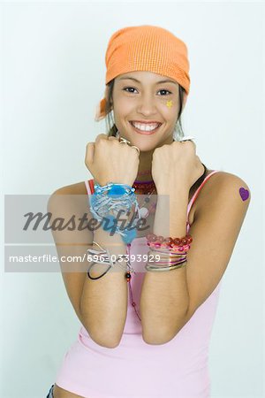 Teen girl wearing lots of accessories, holding up forearms, smiling at camera, portrait