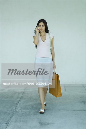 Woman carrying shopping bags, using cell phone, full length portrait