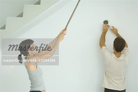 Woman painting ceiling with roller extension, man changing light bulb