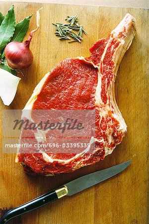 Raw steak on cutting board with herbs and knife, high angle view