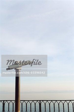 Pay binoculars looking over railing at horizon over water