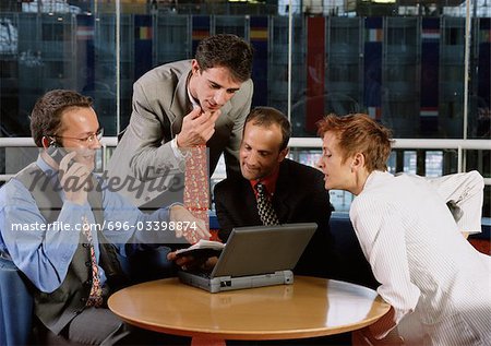 Three men and a woman sitting at table, looking at laptop computer