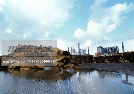 Scrap iron at edge of water, power plants in background