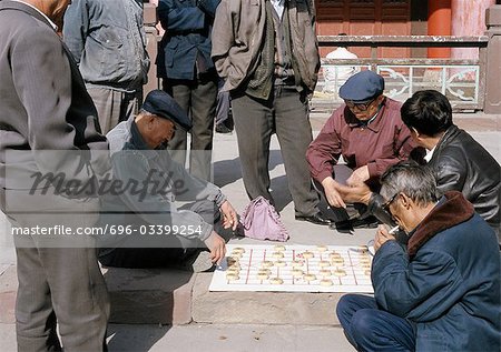 China, Xinjiang Province, Urumqi, group of men sitting on sidewalk playing xiangi on pavement
