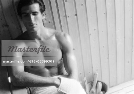 Bare-chested man leaning against wall in sauna with eyes closed, b&w