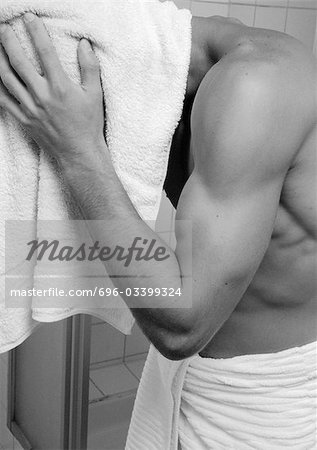 Barechested man with towel around waist towel-drying hair, close-up, b&w