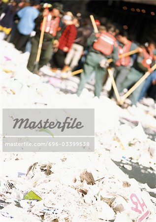 People sweeping ground covered in garbage, blurred