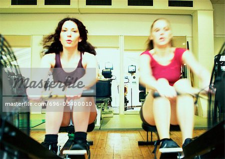 Women using rowing machines in gym, front view