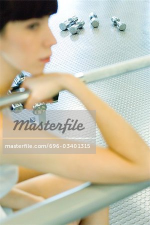 Woman sitting in weight room, focus on dumbbells on floor in background
