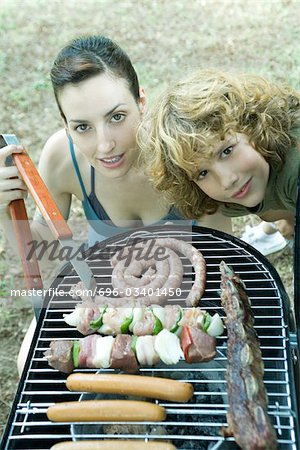 Family having cookout, woman and boy next to barbecue, smiling at camera