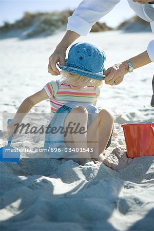 Woman adjusting girl's sunhat on beach
