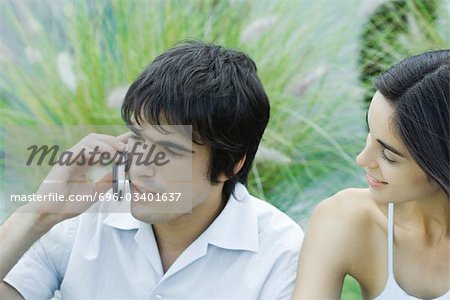Young man using cell phone while girlfriend waits