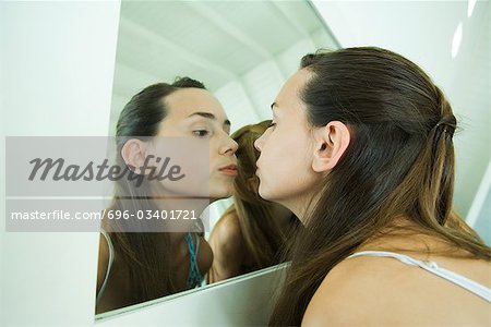 Teenage girl looking at self in mirror, kissing her reflection