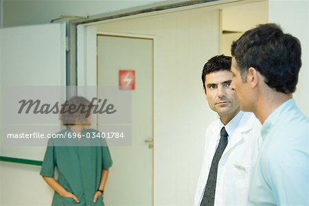 Man standing with doctor in hospital, side view, woman in background
