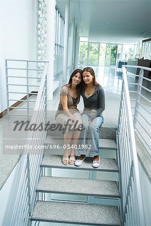 Mother and teenage girl together, sitting on steps, smiling at camera, full length
