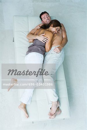 Couple lying on chaise longue together, snuggling and smiling, full length, view from above