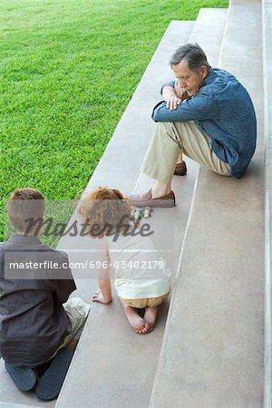 Grandfather and two grandchildren playing with toy cars together on stairs, high angle view