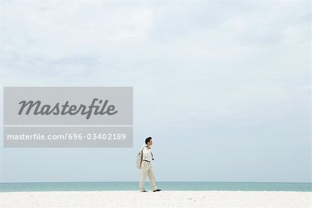 Man in suit walking along beach, side view