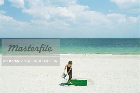Girl watering square of artificial turf on beach, high angle view