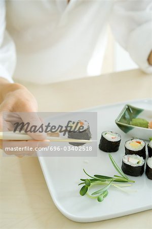 Person using chopsticks to pick up a sushi roll, cropped view