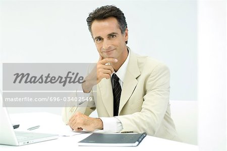 Business executive sitting at desk, smiling at camera, portrait