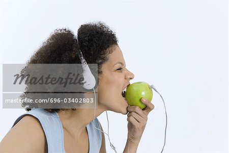 Woman wearing headphones plugged into apple, biting into apple, profile