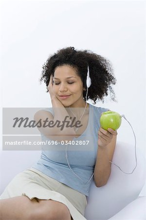 Woman listening to headphones connected to apple, eyes closed