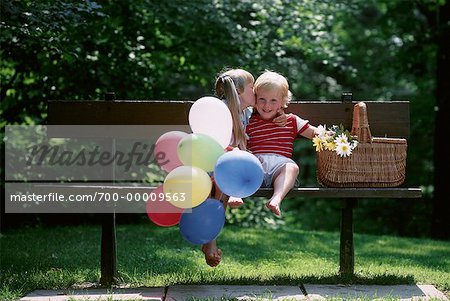 Girl Kissing Boy Sitting On Park Bench