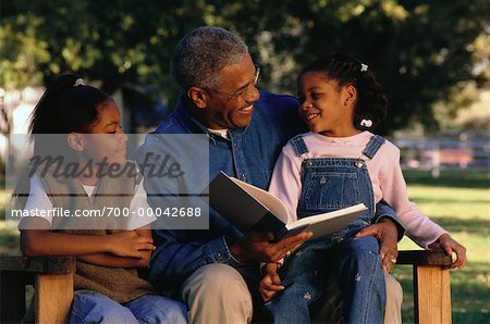 Father Reading to Daughters Sitting on Park Bench