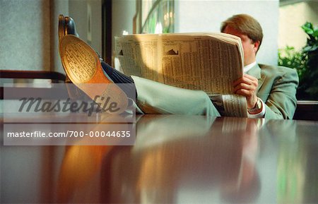Businessman Reading Newspaper With Feet on Desk