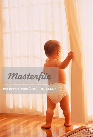 Toddler Wearing Diaper Stands Looking Out Window by Stocksy