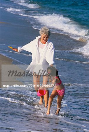 Grandmother and Granddaughter Running in Surf on Beach