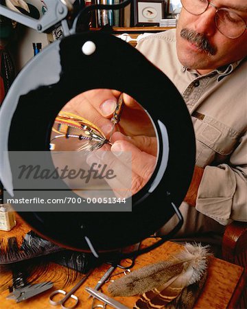 Male Flytier Tying Fishing Fly Under Magnifying Glass - Stock Photo