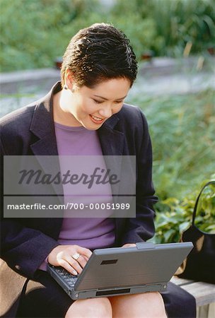 Businesswoman Sitting on Bench Using Laptop Computer Outdoors