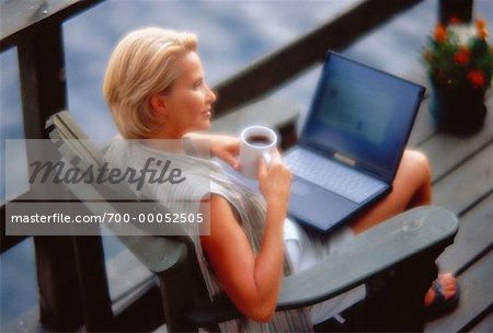 Mature Woman Sitting in Chair on Dock with Laptop Computer and Mug