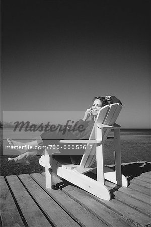 Woman Sitting in Adirondack Chair On Dock Using Cell Phone
