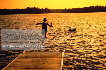 Back View of Girl Jumping into Water from Dock at Sunset