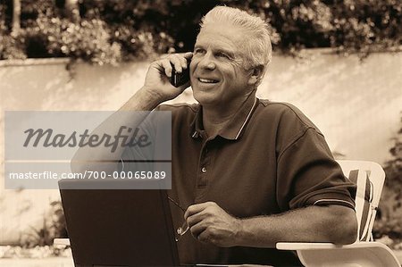 Mature Man Using Cell Phone And Laptop Computer Outdoors