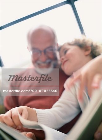 Grandfather and Granddaughter Sitting on Sofa, Reading Book