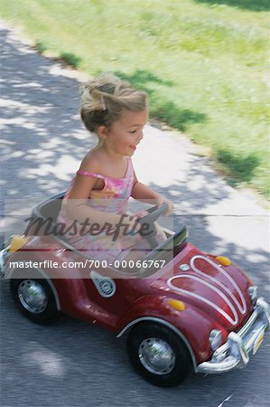 Girl Driving in Toy Car on Sidewalk