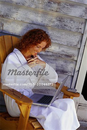 Woman in Bathrobe, Sitting in Chair on Porch Using Laptop