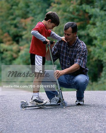 Father Helping Son Ride Scooter Outdoors, Ontario, Canada