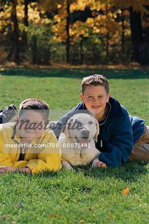 Portrait of Two Boys Lying in Field with Dog in Autumn