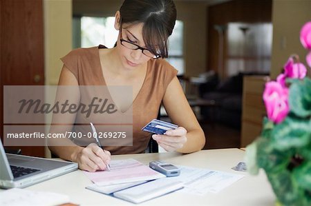 Woman Writing on Bill Holding Credit Card