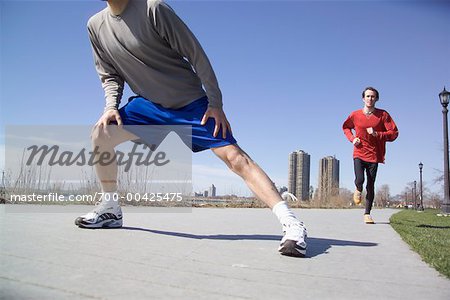 Man Stretching in Front of Other Man Jogging