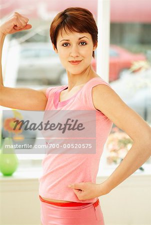 Woman flexing biceps and smiling - Stock Photo - Masterfile